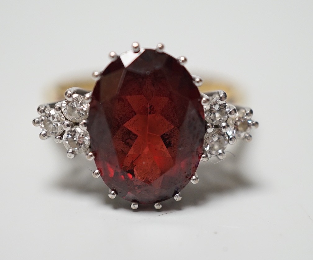 A modern 18ct gold and oval cut garnet set dress ring, with six stone diamond set shoulders, size M/N, gross weight 4.8 grams.